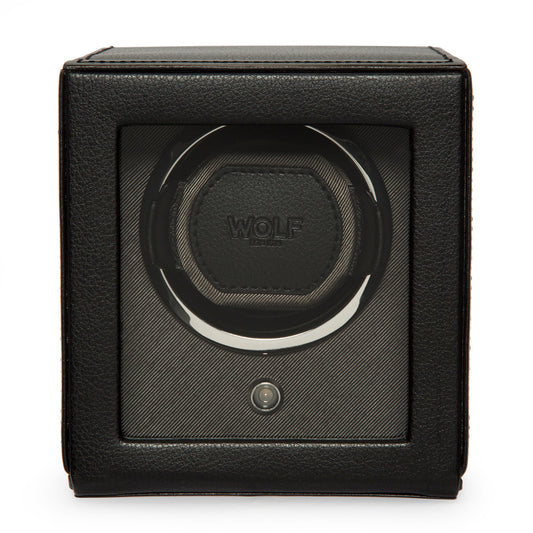 The WOLF 1834 Cub Winder With Cover, a black Wolf watch winder, features a transparent front and a sleek vegan leather exterior. Its empty interior is specifically designed to hold one watch. The square-shaped device boasts a central circular mechanism for bi-directional automatic winding.