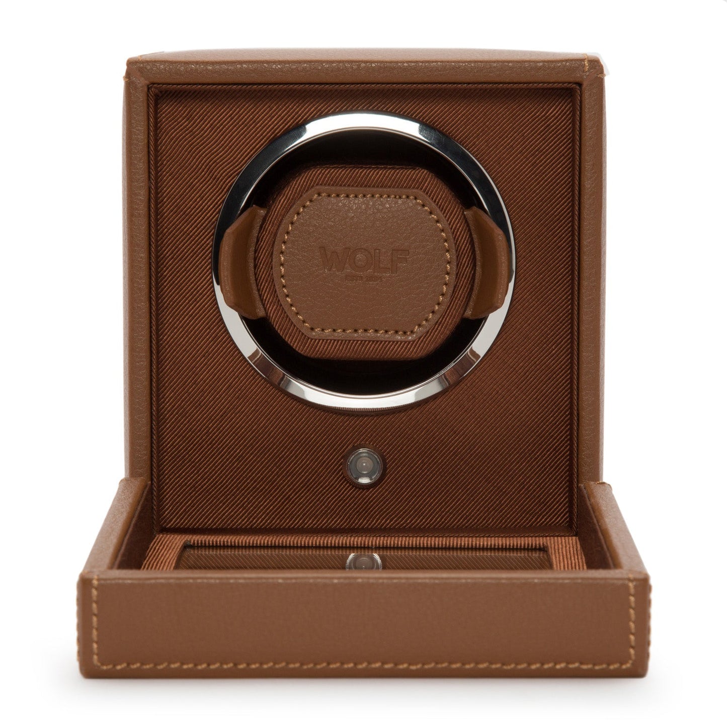 The WOLF 1834 Cub Single Watch Winder With Cover features a brown design with leather details and the "WOLF" logo embossed on the front, housed inside an open box with a textured finish. This elegant, circular watch winder offers customizable rotation programs for optimal timekeeping while securely cradling your watches.
