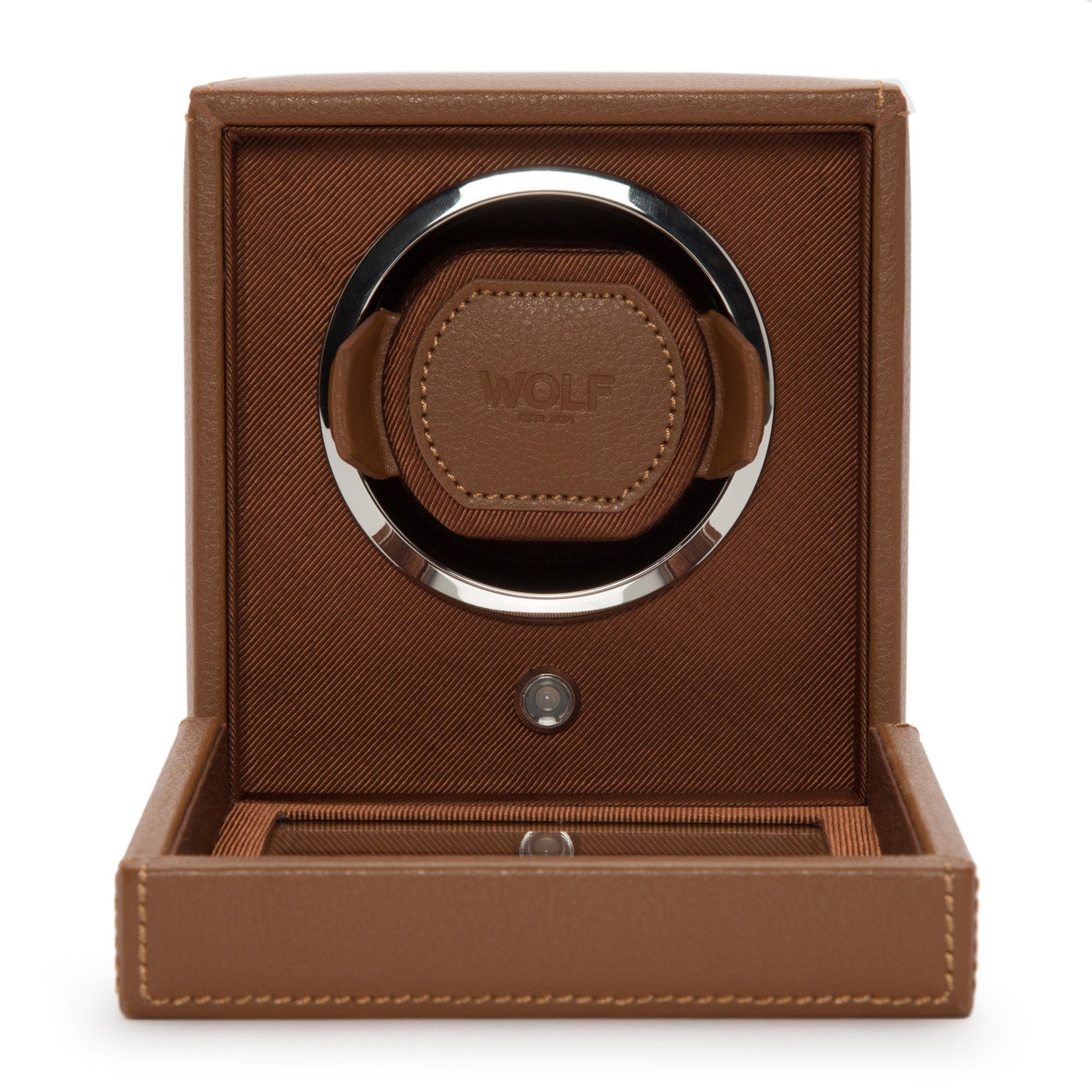 The WOLF 1834 Cub Single Watch Winder With Cover features a brown design with leather details and the "WOLF" logo embossed on the front, housed inside an open box with a textured finish. This elegant, circular watch winder offers customizable rotation programs for optimal timekeeping while securely cradling your watches.