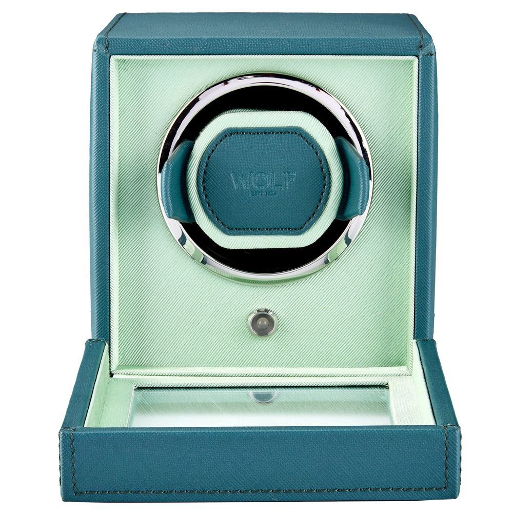 The WOLF 1834 Cub Single Watch Winder in teal features luxurious vegan leather accented with silver, a circular holder, and the “WOLF” logo embossed at the center. With its lid open and a sleek glass panel at the base, it showcases a modern aesthetic.