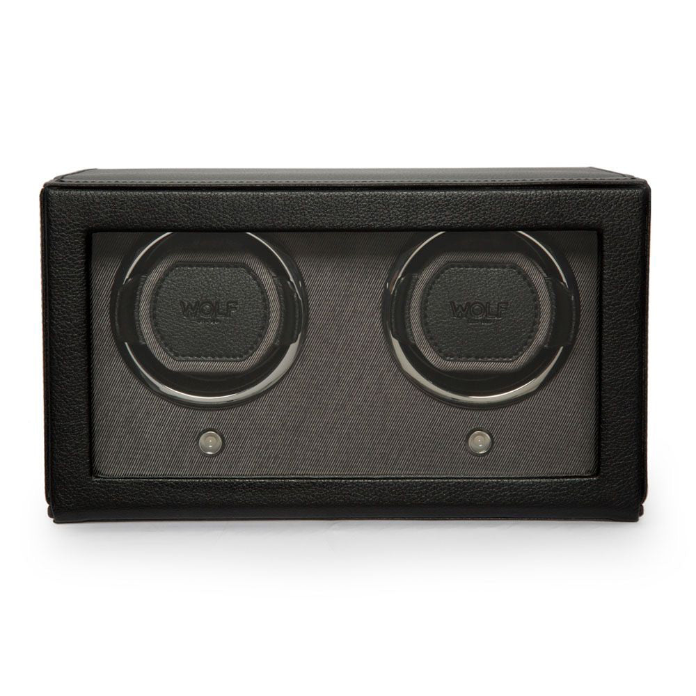 The WOLF 1834 Cub Double Watch Winder With Cover is a sleek black, rectangular accessory crafted with vegan leather. It features two circular winding slots, each showcasing the "Wolf" label and equipped with a patented lock-in cuff. The design is elegantly set against a dark grey fabric background and includes a transparent front panel.