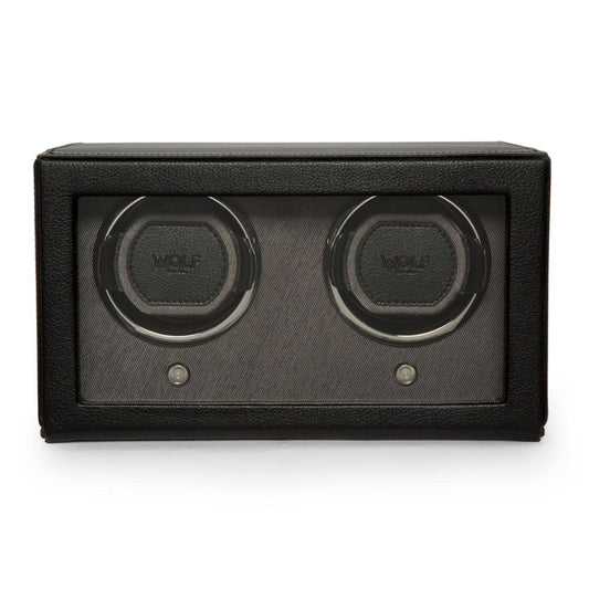 The WOLF 1834 Cub Double Watch Winder With Cover is a sleek black, rectangular accessory crafted with vegan leather. It features two circular winding slots, each showcasing the "Wolf" label and equipped with a patented lock-in cuff. The design is elegantly set against a dark grey fabric background and includes a transparent front panel.