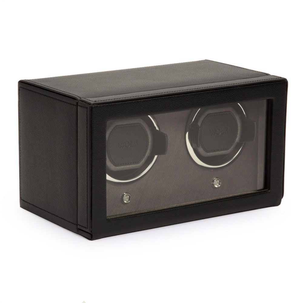 The WOLF 1834 Cub Double Watch Winder With Cover, crafted by WOLF, features a black vegan leather exterior and a glass front that elegantly displays two slots for watches. The inside is lined with soft material, while its sleek and modern design incorporates a patented lock-in cuff to securely and stylishly hold your timepieces.