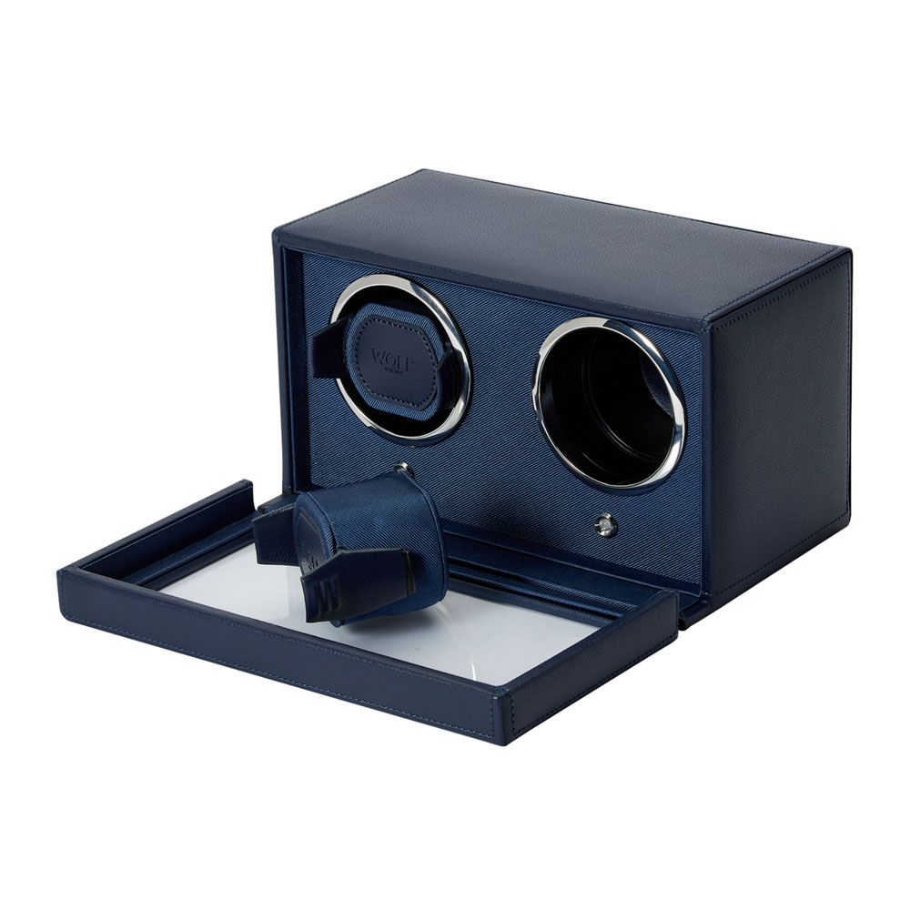 The WOLF 1834 Cub Double Winder With Cover in Navy is a vegan leather watch winder box featuring two circular slots, with one slot housing a watch holder. Its front panel rests open and flat, providing a clear view of the interior and highlighting WOLF’s patented rotation system designed for optimal care of your timepieces.