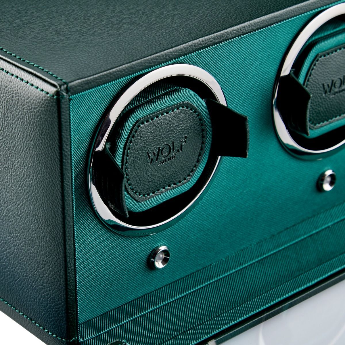 Close-up of the WOLF 1834 Cub Double Winder With Cover Green, a sophisticated green and black watch winder by WOLF, crafted from premium vegan leather with chrome accents. Featuring two winding slots and patented rotation technology, this sleek accessory is showcased on a reflective surface for added elegance.