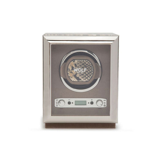 The WOLF 1834 Exotic Single Watch Winder, with its glass front, elegantly displays a timepiece. This silver device boasts a digital control panel and buttons below, known for its precise rotations. Its design is enhanced with top grain cowhide leather accents, while the brand "WOLF" can be seen on the watch within.