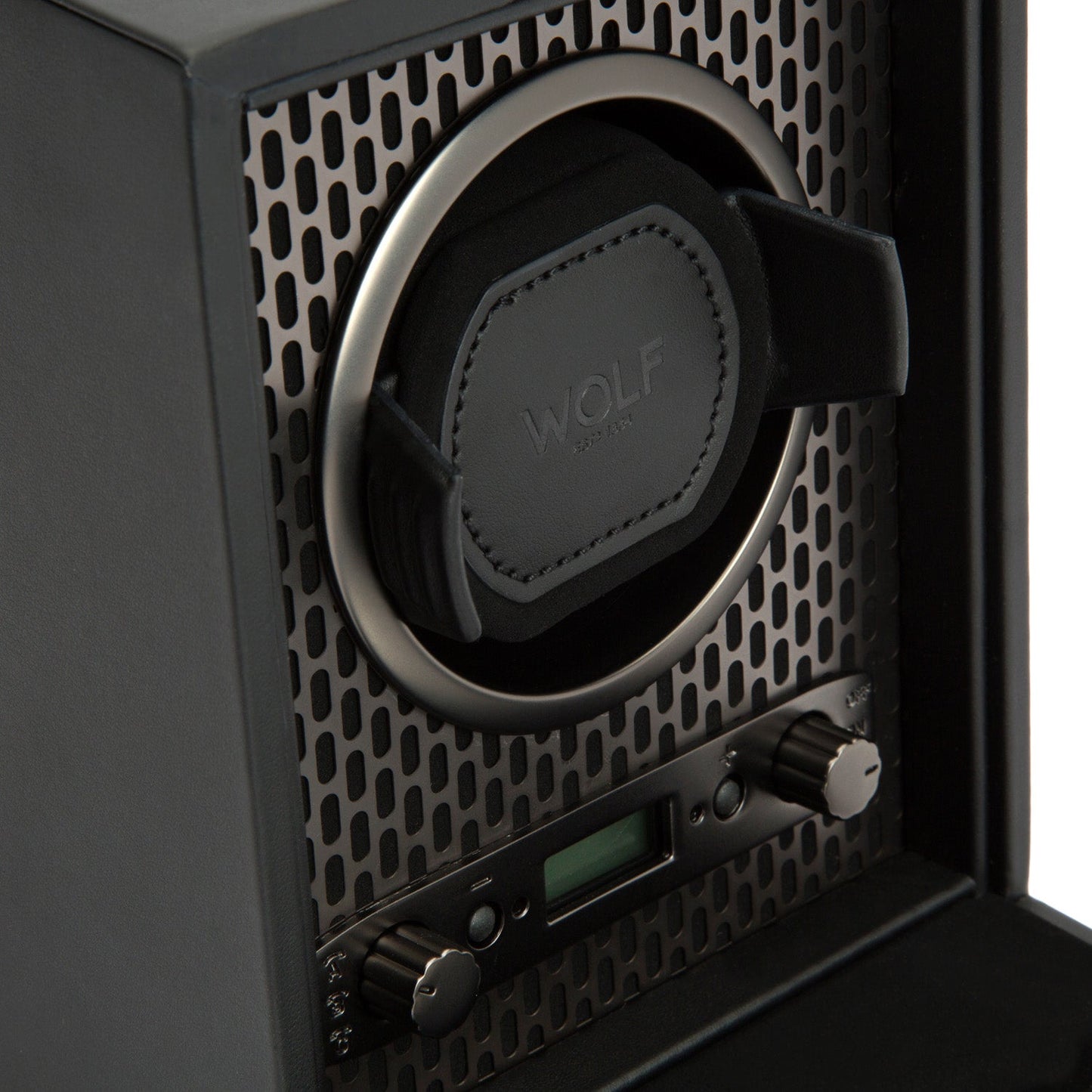 Close-up of the WOLF 1834 Axis Single Watch Winder in black, highlighting its padded circular holder within a mesh-patterned case. Two control knobs offer rotation options, accompanied by a small digital display. The lock-in dynamic cuff ensures your watch stays secure, with "WOLF" embossed on the holder.