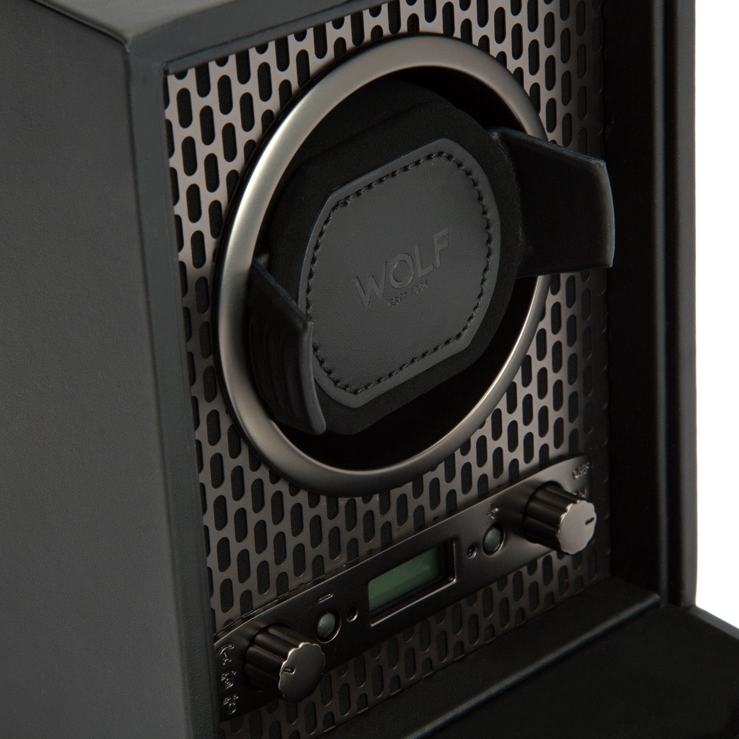 Close-up of the WOLF 1834 Axis Single Watch Winder in black, highlighting its padded circular holder within a mesh-patterned case. Two control knobs offer rotation options, accompanied by a small digital display. The lock-in dynamic cuff ensures your watch stays secure, with "WOLF" embossed on the holder.