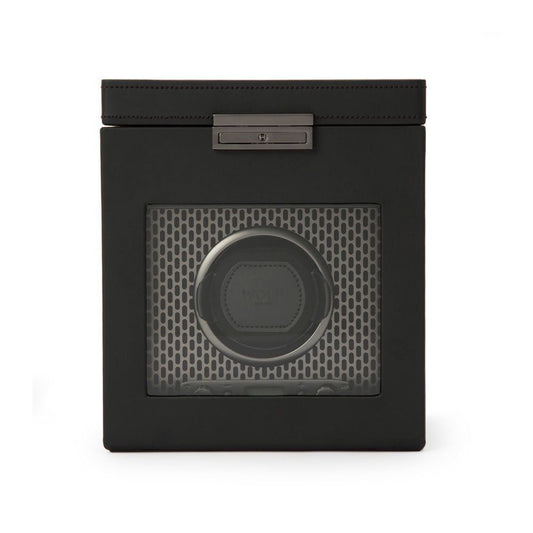 The WOLF 1834 Axis Single Watch Winder With Storage by WOLF is a black, square device with a clear front panel. It showcases a circular mount that holds the watch against a stylish honeycomb-patterned interior. Designed for optimal display, it offers rotation options and includes a metallic latch on top to elegantly secure the lid.