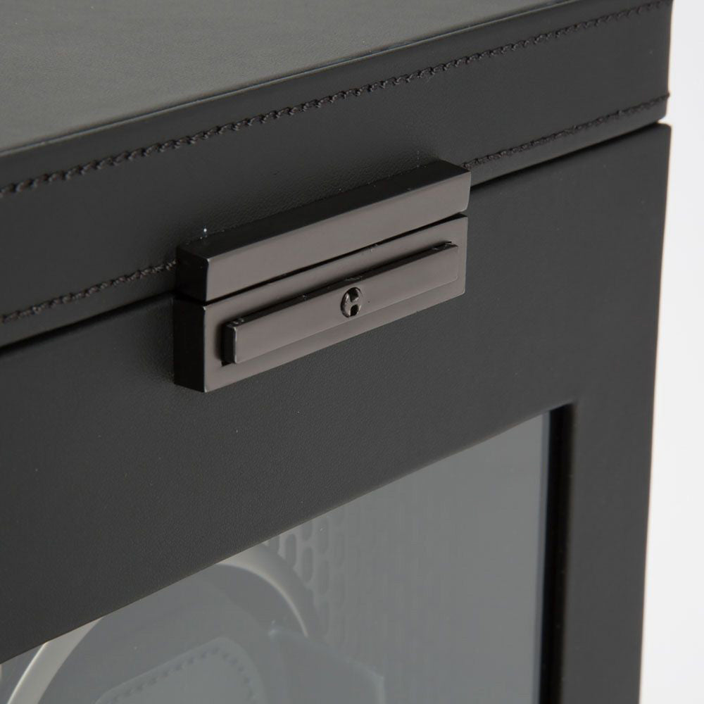 A close-up of the WOLF 1834 Axis Single Watch Winder With Storage, showcasing a sleek black glass exterior accented by a modern metallic handle with a keyhole for secure locking. Inside, the visible gear mechanism mirrors the precision and sophistication found in WOLF winders, providing an array of rotation options. The cabinet exemplifies a contemporary, minimalist design.