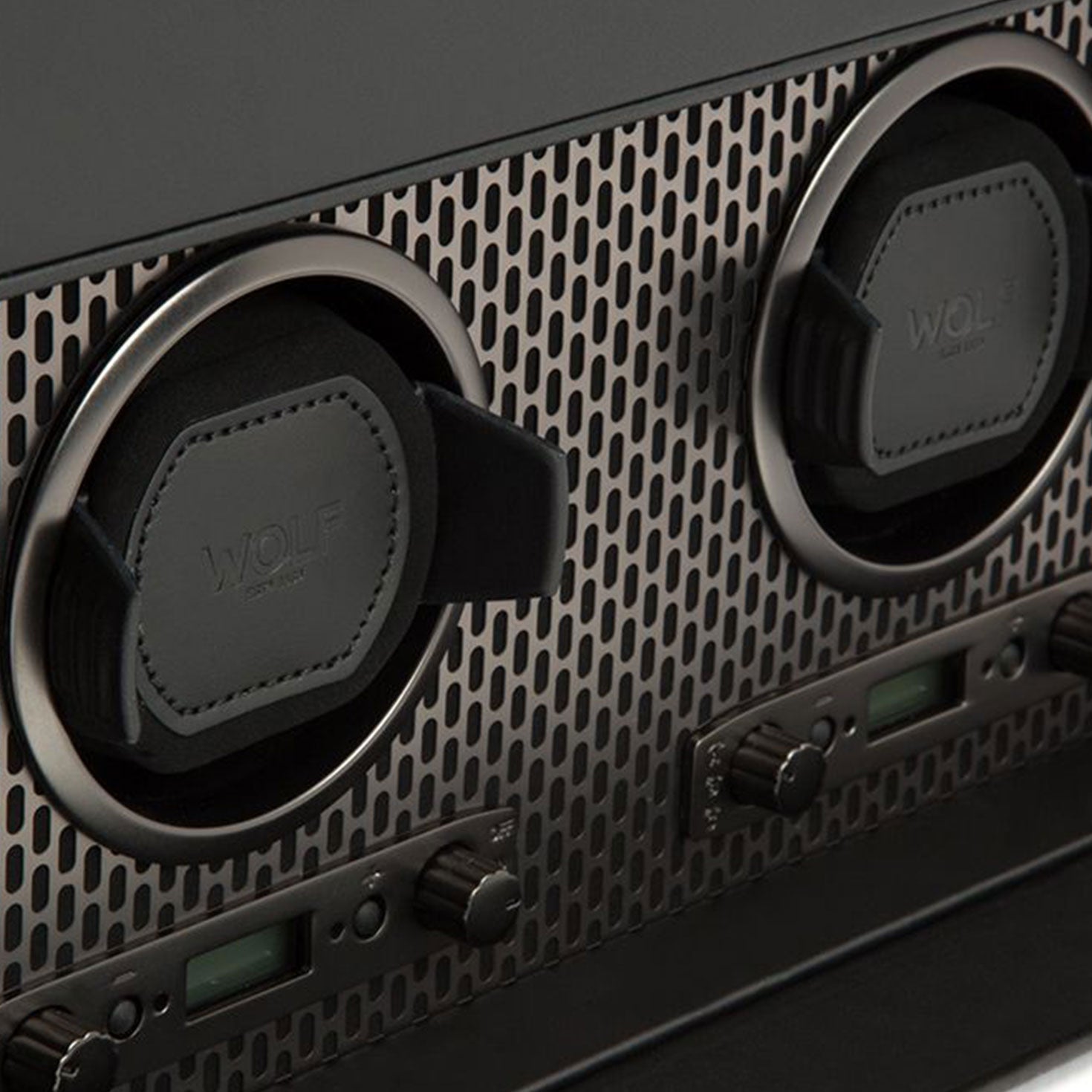 Close-up of the WOLF 1834 Axis Double Winder With Storage showcasing two circular winders from the Wolf brand, seamlessly integrated into a perforated grille pattern. Made from powder-coated steel, this sleek industrial design features two control knobs and small digital displays for optimal watch storage.