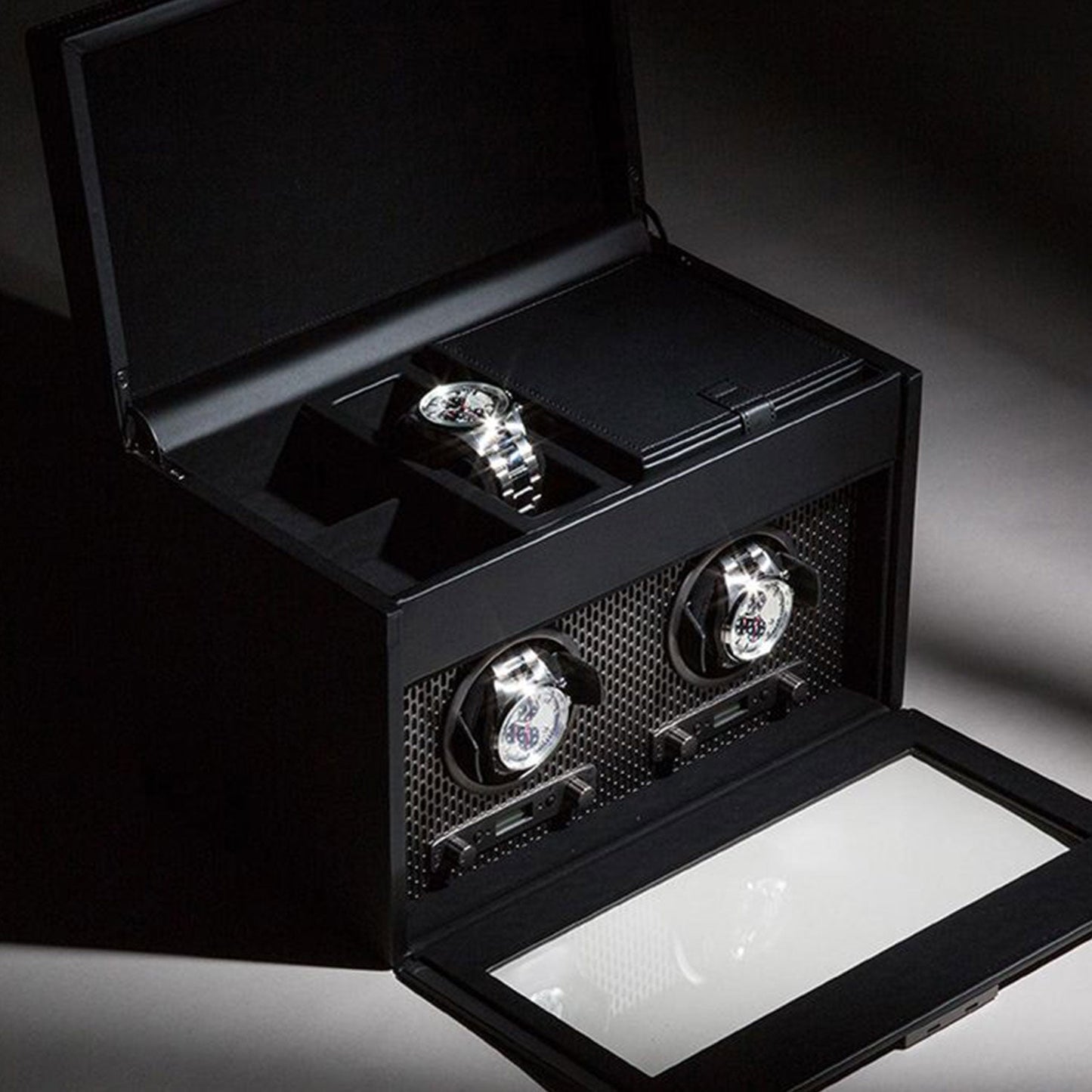 The WOLF 1834 Axis Double Winder With Storage, a sophisticated watch box by WOLF, features an open lid that displays three luxury watches. The design embodies exquisite watch storage with two watches securely mounted on rotating holders and one resting flat in the top compartment with a glossy finish, ensuring the utmost security for your timepieces.