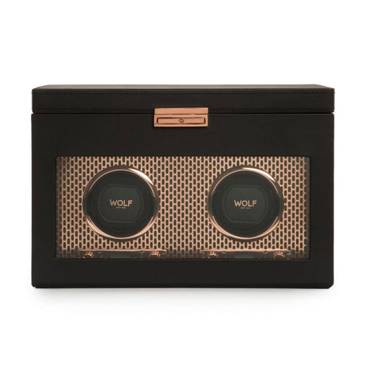 The WOLF 1834 Axis Double Winder With Storage is a black, rectangular watch winder featuring winding modules and a transparent front that highlights two circular compartments labeled "WOLF." The design includes a gold mesh-like patterned background and an elegant metal latch made from copper-plated steel at the top center.