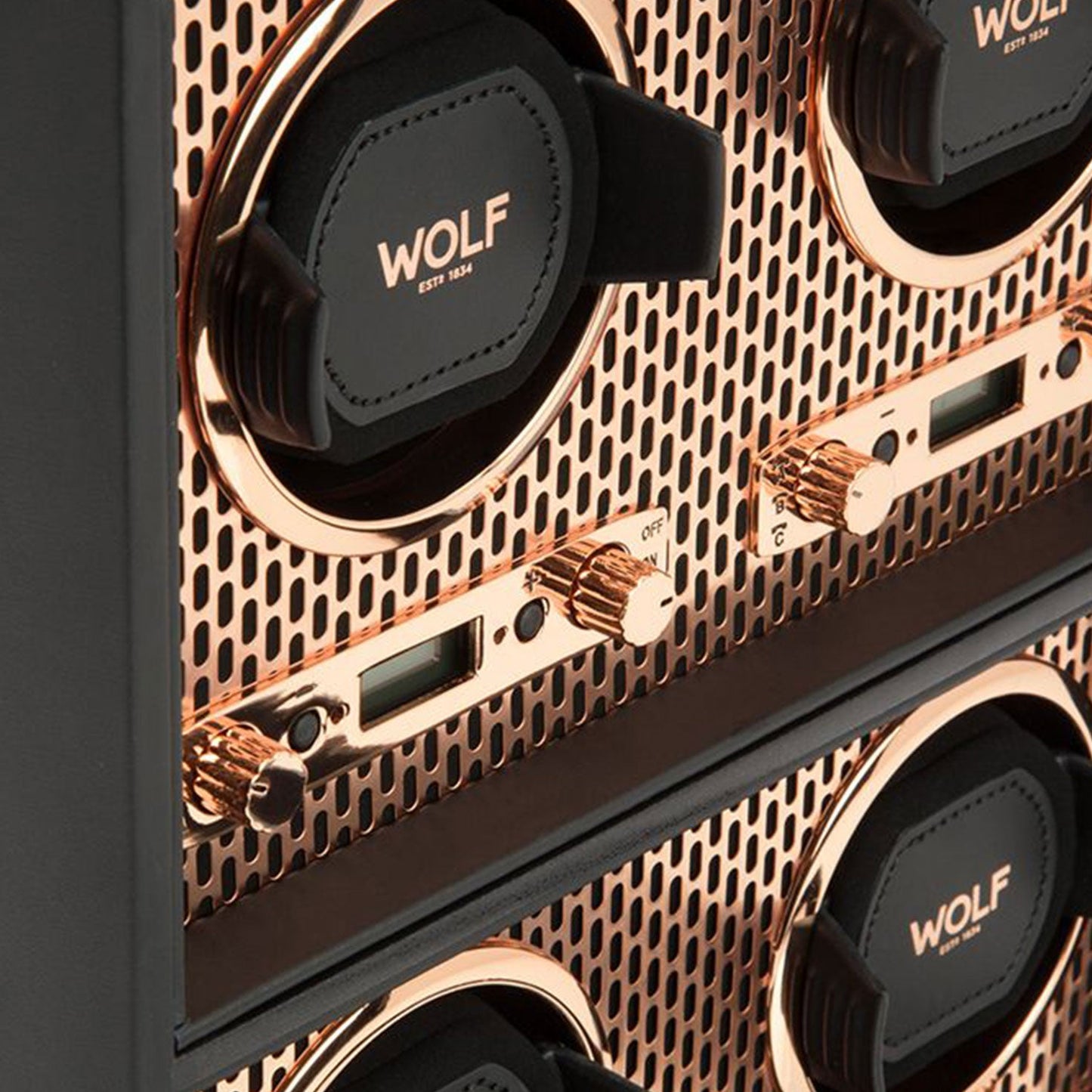 A close-up view of the WOLF 1834 Axis 4 Piece Winder highlights its luxury design with multiple compartments and prominent "WOLF" branding. Its sophisticated look is enhanced by a copper-plated metal grille and control knobs, making it perfect for elegantly safeguarding your timepieces.
