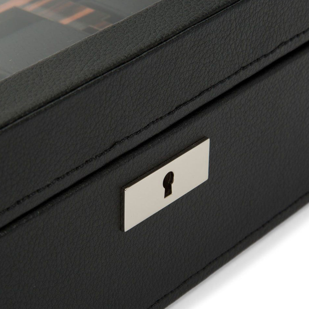Here's a revised version of the sentence using the provided product data:

A close-up of the WOLF 1834 Roadster 10 Piece Watch Box in black vegan leather, featuring a silver metallic lock plate. The textured surface complements its design, while a transparent lid partially reveals the watch storage inside.