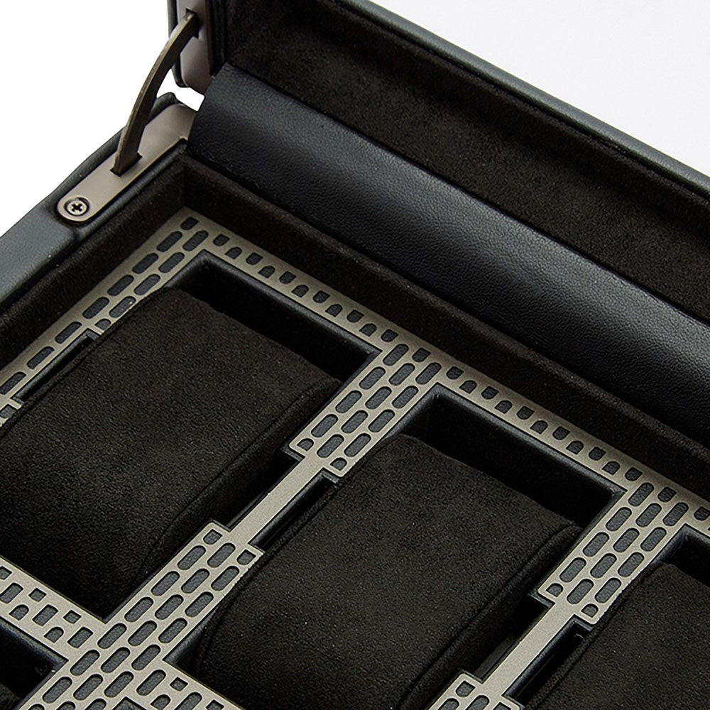 A close-up of the WOLF 1834 Axis 10 Piece Watch Box reveals an open case with multiple empty slots lined with soft black material, designed to securely hold both traditional and smart watches. The interior is bordered with a textured metallic frame and features lock and key security for added peace of mind.
