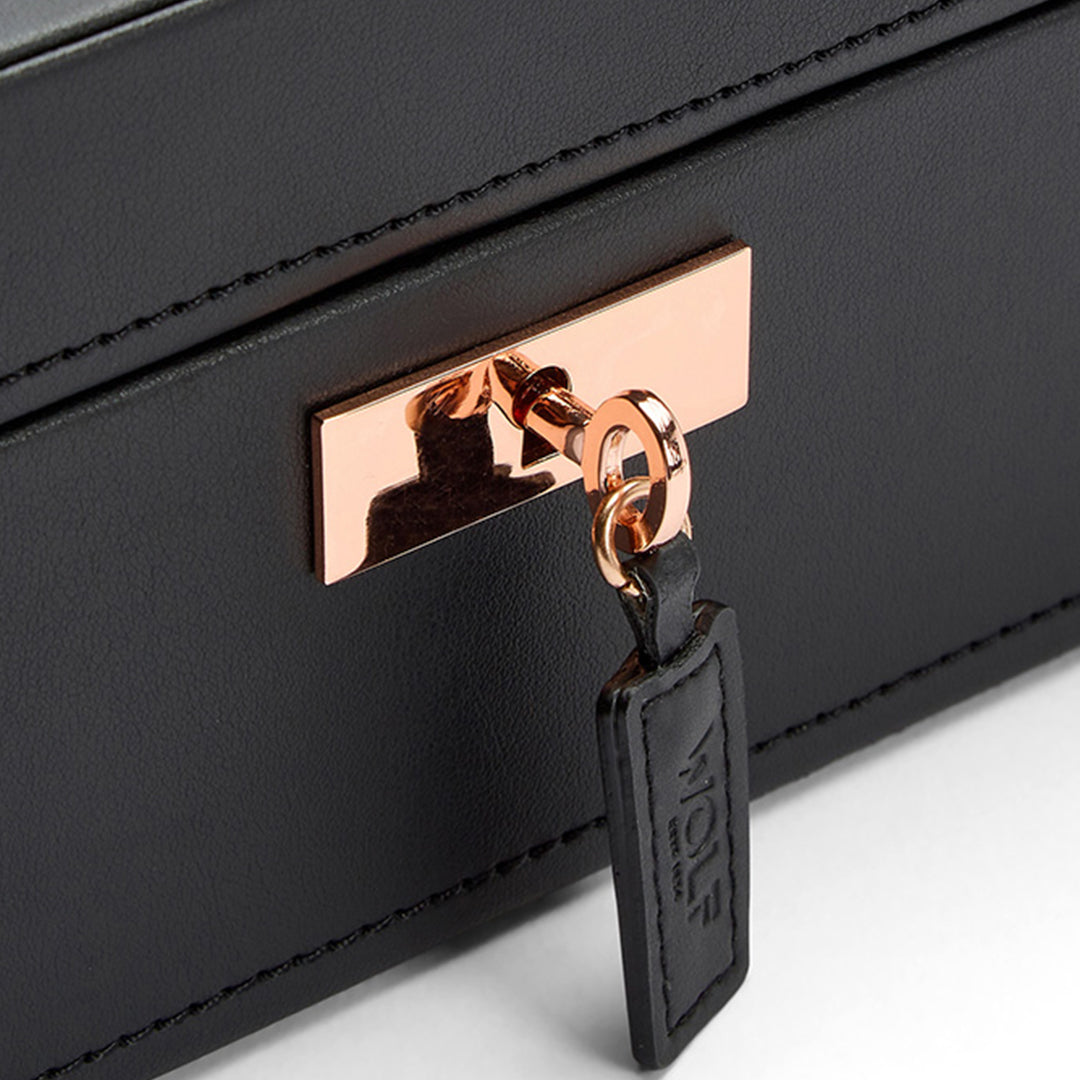 A close-up of the WOLF 1834 Axis 10 Piece Watch Box in black leather showcases its elegant rose gold lock. Attached is a black leather keychain embossed with the brand name "WOLF," accentuating its lock and key security feature. The sophisticated design, featuring suspended watch cushions, exudes luxury and elegance, making it perfect for refined watch storage.