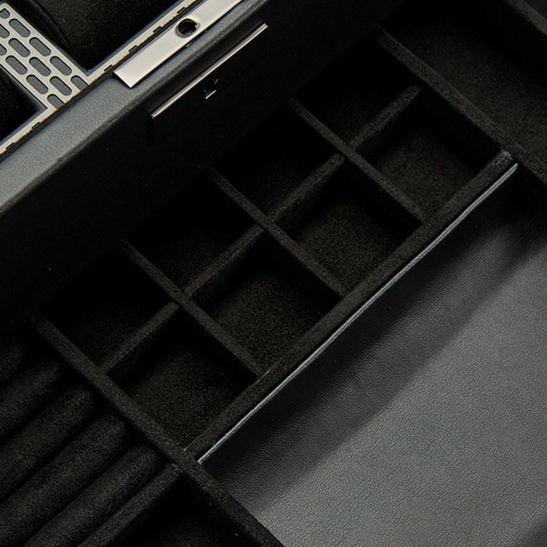 The close-up showcases the WOLF 1834 Axis 10 Piece Watch Box with Drawer, featuring multiple compartments of varying sizes ideal for watch storage. A metallic clasp is present at the top, suggesting lock and key security, while the right side is adorned with a smooth leather-like material.