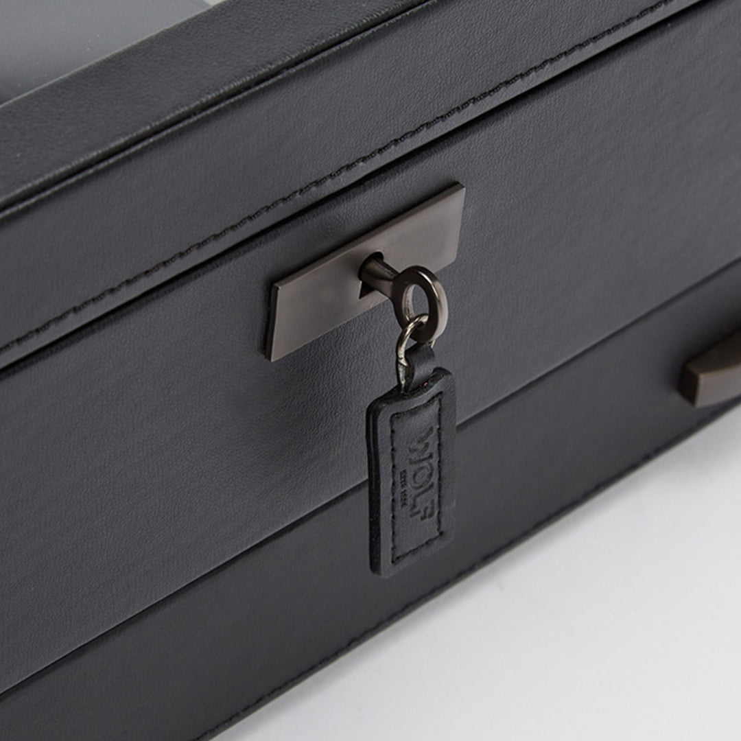 The close-up showcases the WOLF 1834 Axis 10 Piece Watch Box with Drawer, featuring a black leather exterior and lock-and-key security. A key with a rectangular leather keychain embossed with text is inserted into the metal lock, ensuring your valuables are securely and stylishly stored by WOLF.