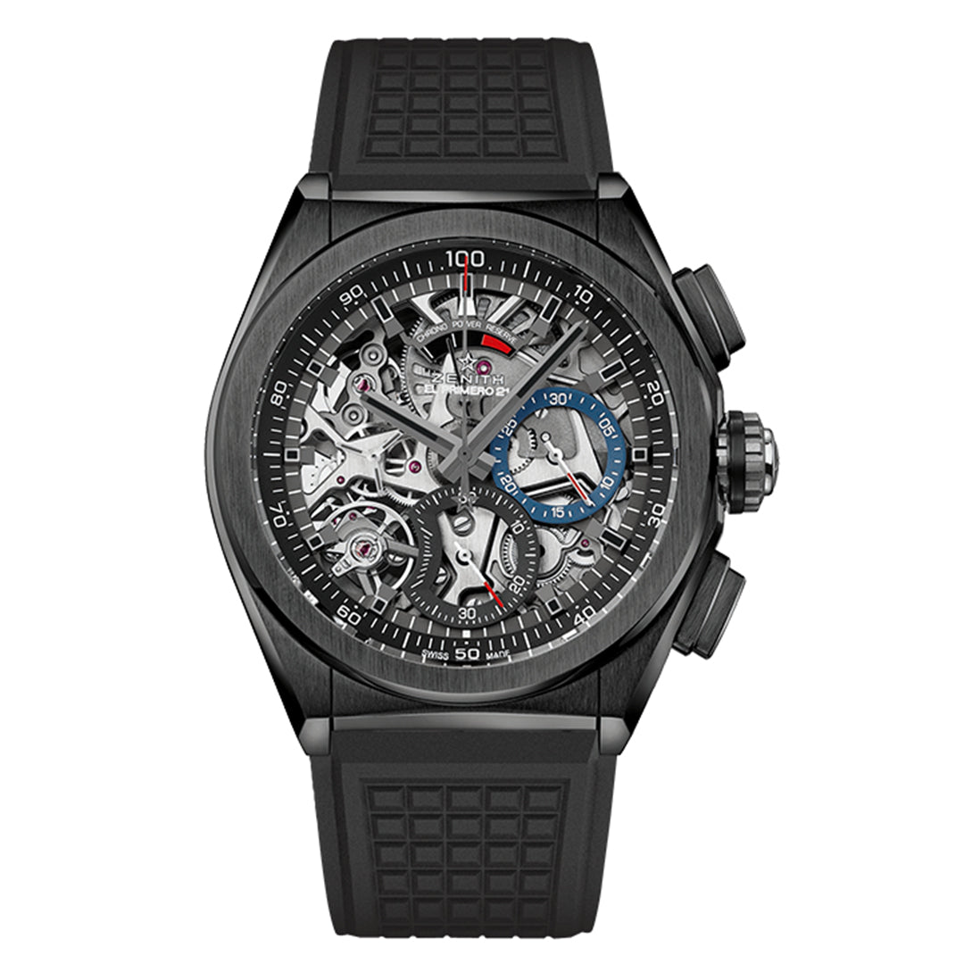 The Zenith Defy El Primero 21 44mm Watch is a sleek black timepiece with a skeleton dial revealing intricate gears. It has a chronograph, blue subdial, and black rubber strap, blending modern style with mechanical complexity.