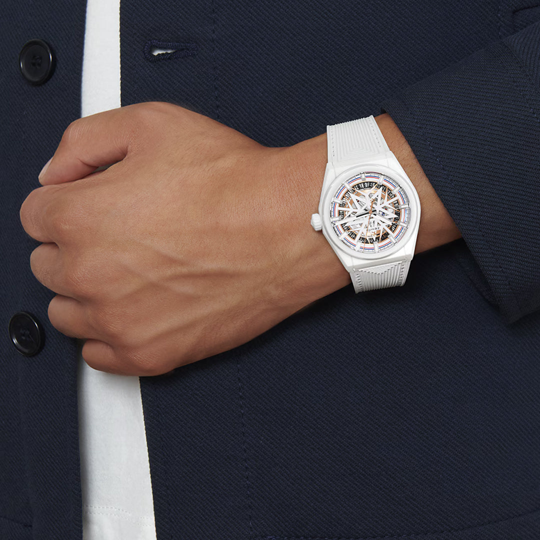 A person in a dark blue jacket and white shirt showcases the stylish ZENITH Defy Classic Elite 670 41mm watch by Zenith. The intricate design on its face with a wide white ceramic band is prominently displayed on their left wrist.