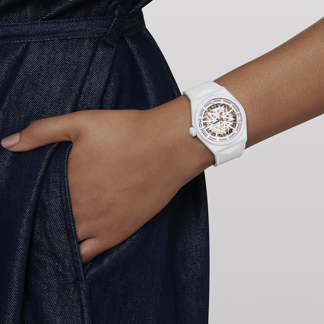 A person sporting the Zenith Defy Classic Elite 670 41mm watch, featuring a transparent skeletal dial and Elite automatic movement, has their hand in the pocket of a dark denim outfit against a plain light grey background.