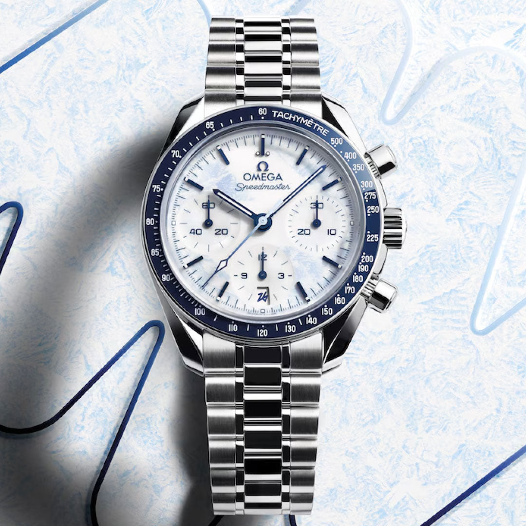 The OMEGA Speedmaster 38 Co-Axial Chronometer Chronograph 38mm Milano Cortina 2026 Edition watch features a white dial, blue bezel, silver bracelet, date display, and three subdials. It is set against a textured white and blue background.