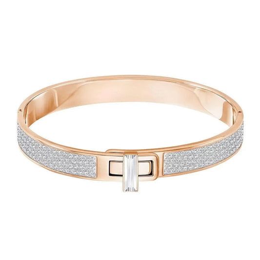 The Swarovski Gave Bangle is a sophisticated accessory, showcasing a gold band embellished with shimmering crystals and tiny diamonds. It is highlighted by a striking rectangular gemstone in the center, providing a refined design that seamlessly enhances any outfit.