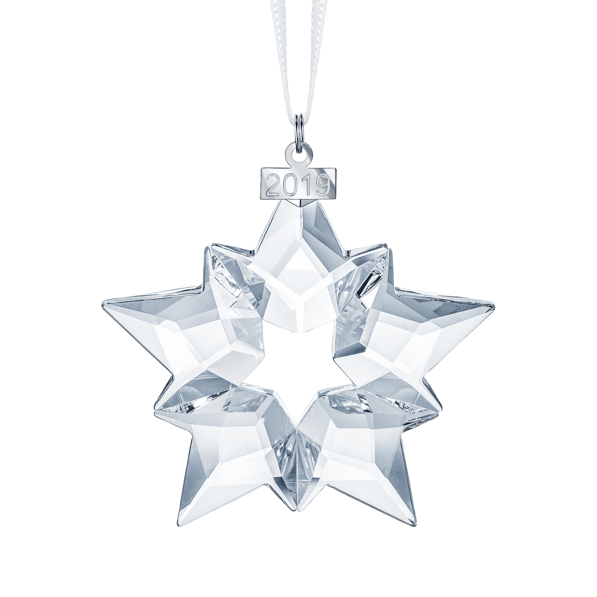 A clear, eight-pointed faceted crystal star ornament from Swarovski hangs from a white ribbon. A small silver tag at the top displays “2019.” The Swarovski Annual Edition Ornament 2019 sparkles beautifully against the plain white background and is available through Raffi Jewellers.