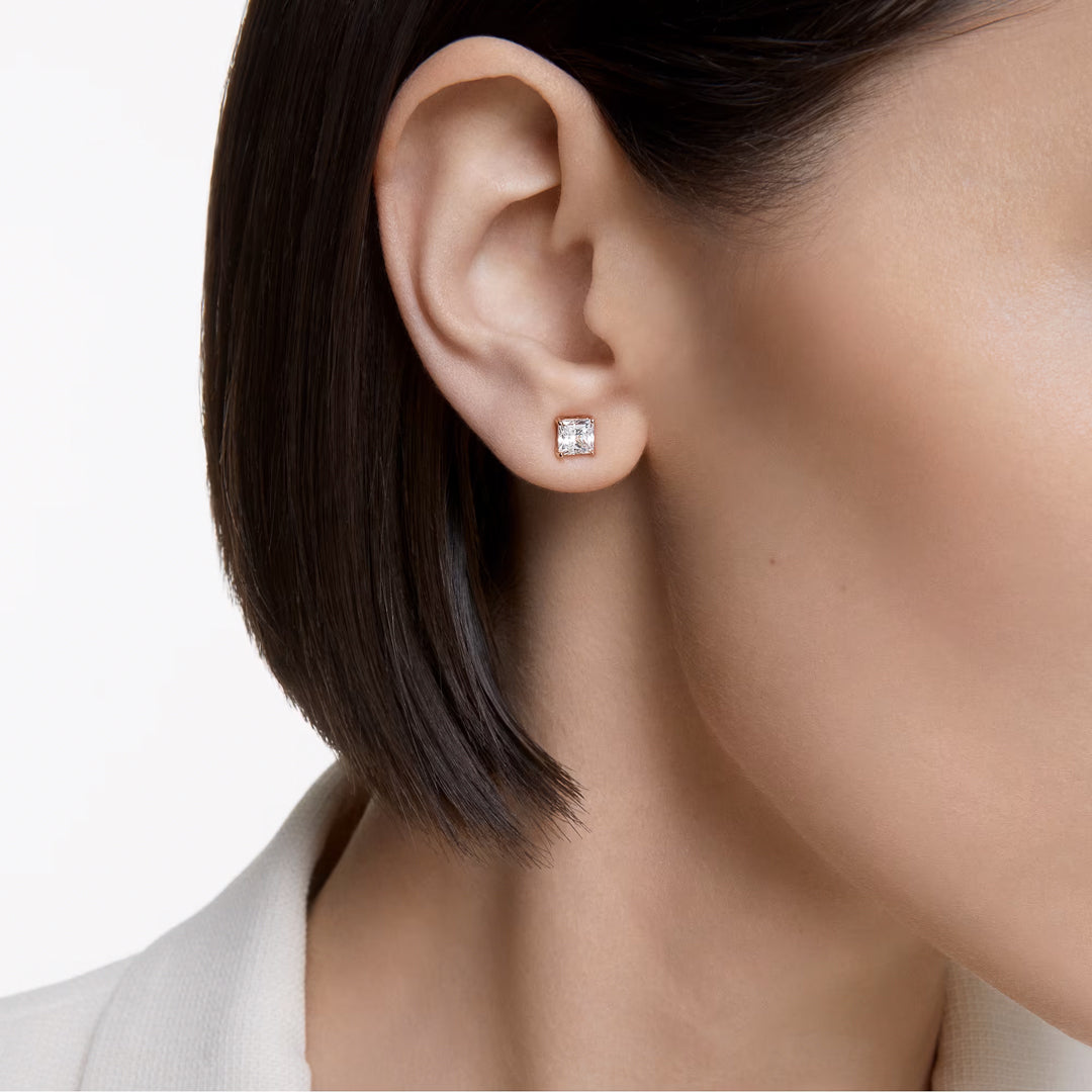 Close-up of a person with short, dark hair wearing the delicate Swarovski Stilla Attract Stud Earrings in rose gold. The background is white, and the person is dressed in a light-colored, collared shirt.