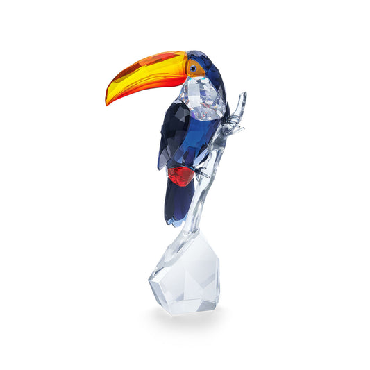 The Swarovski Toucan Crystal Home Décor by Swarovski showcases a stunning crystal sculpture of a toucan with a vibrant orange and yellow beak, deep blue body, and red accent on its tail, all elegantly set on a faceted clear crystal base.