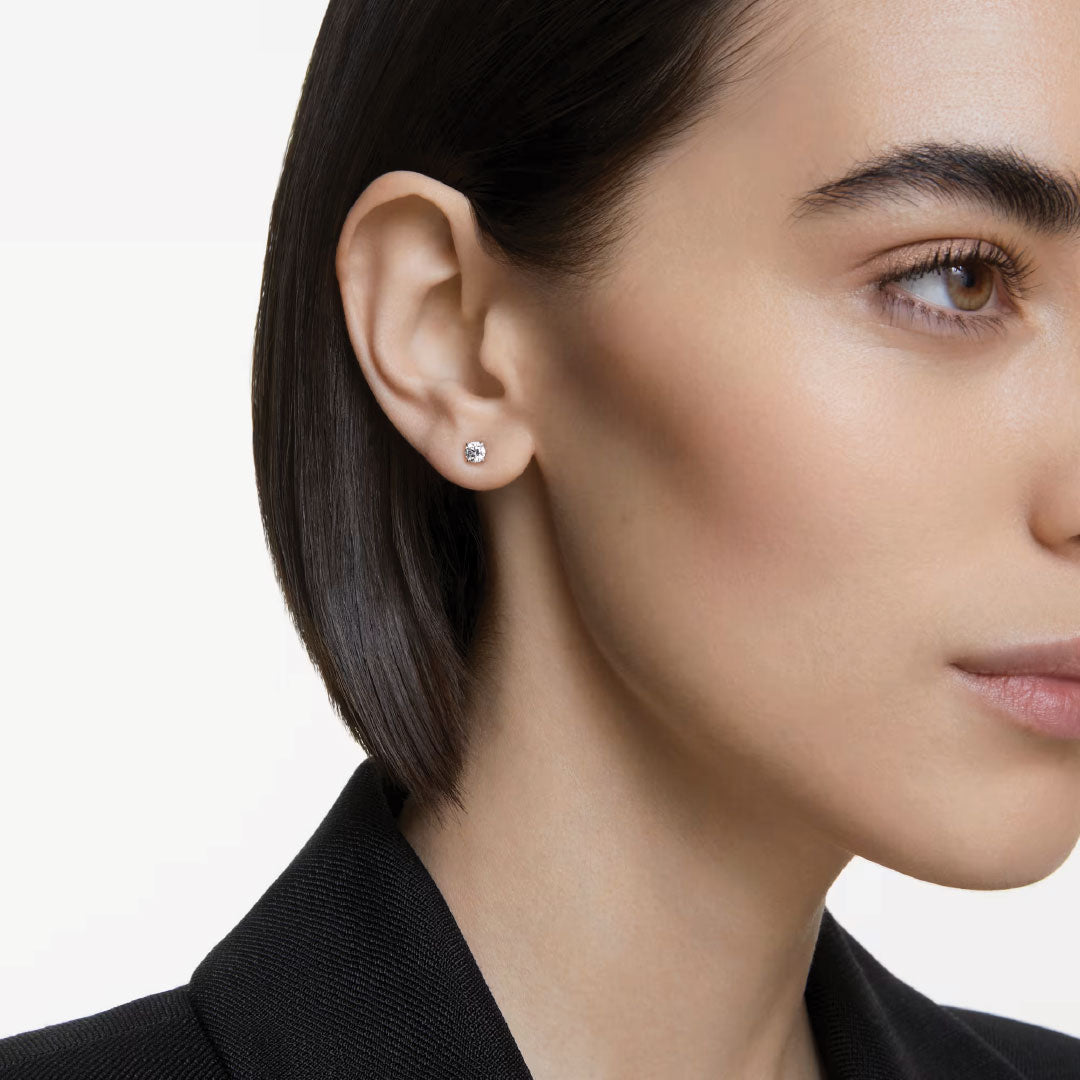A person with short, dark hair wears a small, sparkling Swarovski Stilla Attract Stud Earring in their left ear. They are dressed in a black jacket against a plain, light background, captured in a side profile view.