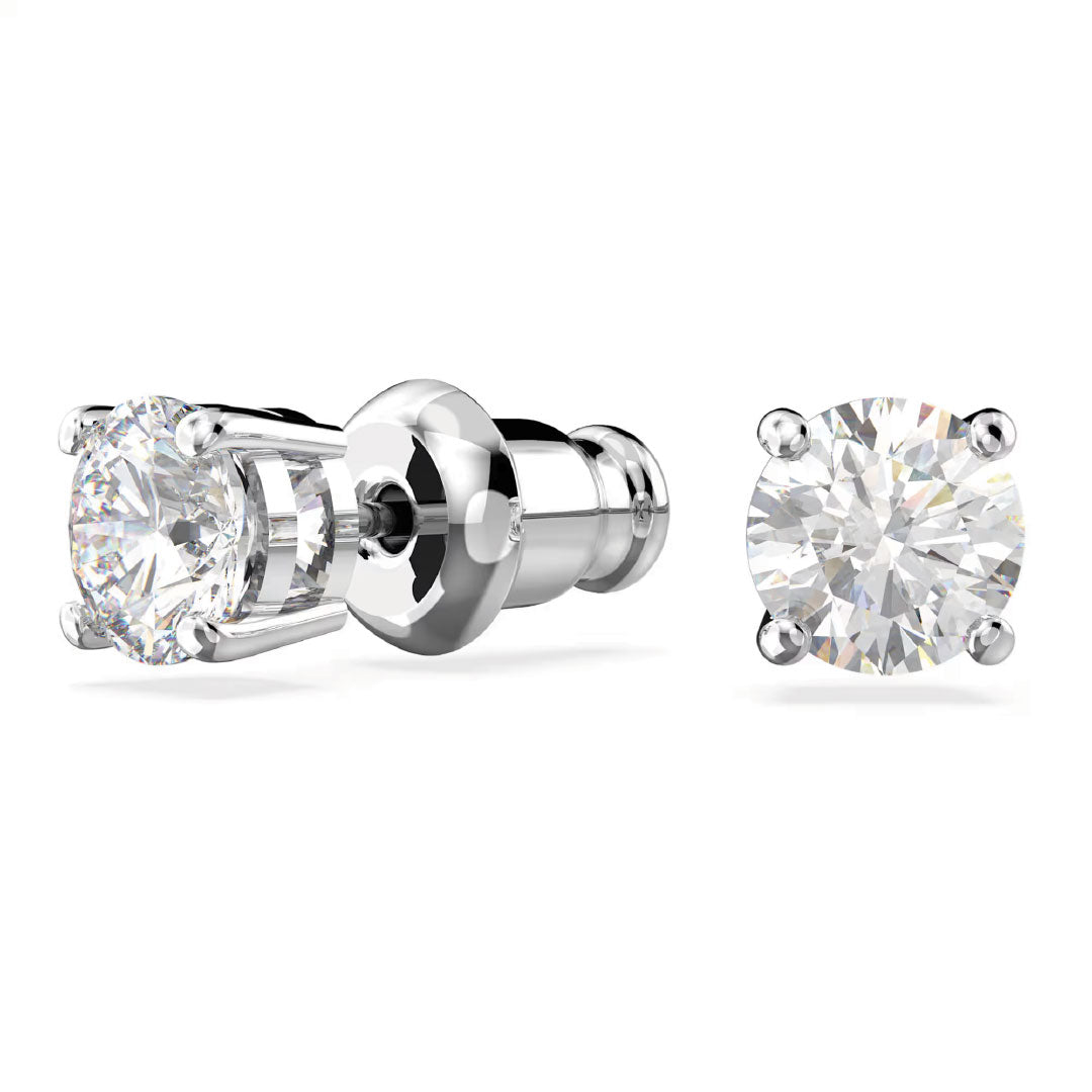 The Swarovski Stilla Attract Stud Earrings, crafted by Swarovski, showcase two rhodium-plated stud earrings that glisten brilliantly. Each earring is set in a four-prong metal base and features a round, brilliant-cut diamond on a white background with secure backings for both front and side view display.