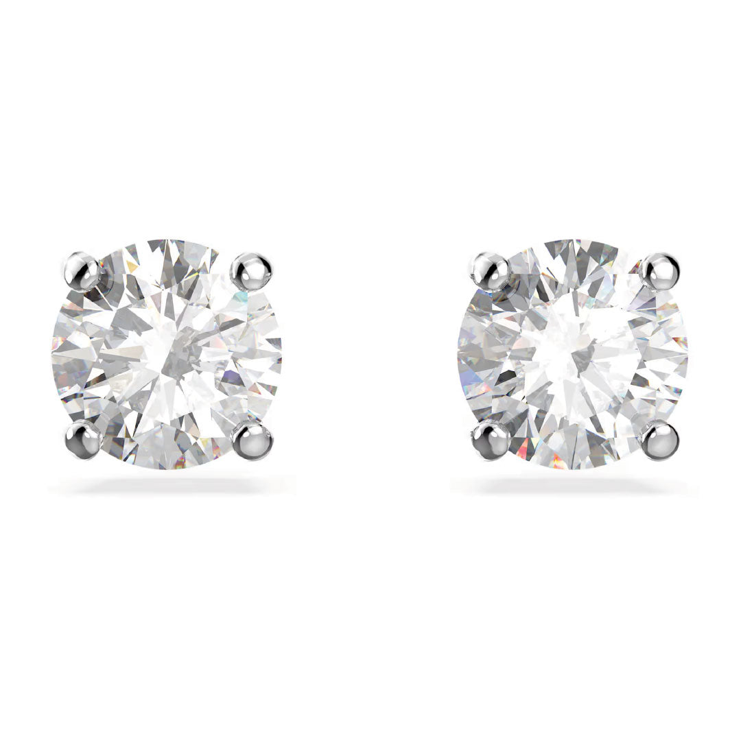 A close-up image features the Swarovski Stilla Attract Stud Earrings, showcasing two round diamonds encased in rhodium-plated silver prongs on a pristine white backdrop. The diamonds exude a clear and sparkling brilliance, highlighting their exceptional clarity, typical of exquisite Swarovski craftsmanship.