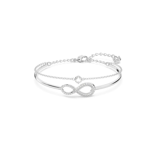 Introducing the Swarovski Infinity Bangle: a delicate silver bracelet that showcases an elegant infinity symbol embellished with sparkling stones. This bracelet is enhanced by rhodium plating and adorned with genuine Swarovski crystals. It features a fine chain and an adjustable clasp for a secure fit.