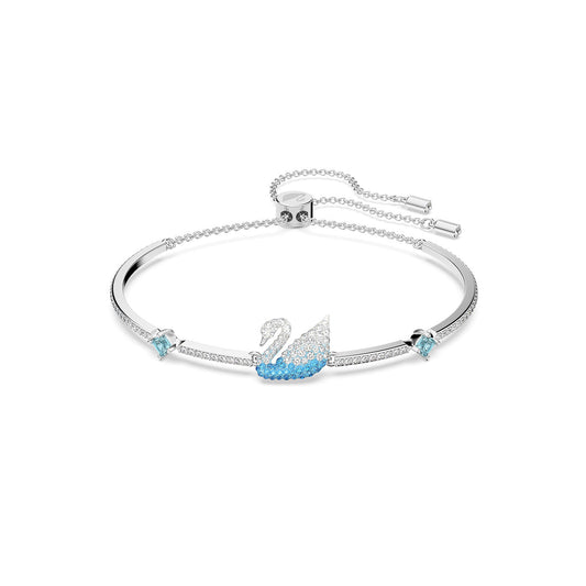 The Swarovski Iconic Swan Bangle by Swarovski is an elegant piece featuring a silver band and a central swan motif, embellished with Swarovski crystals and blue accents. It includes a sliding closure with dangling ends for adjustable sizing.