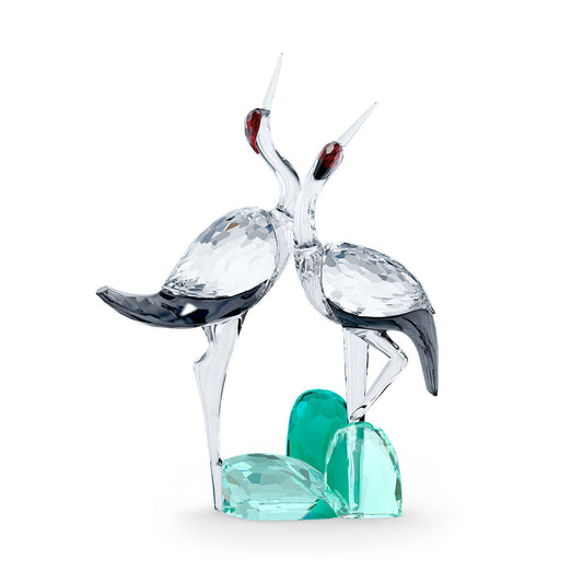 Introducing the Swarovski Among Blue Mountains Singing Cranes Home Décor, a stunning crystal piece from Swarovski. This depiction features two stylized cranes with elongated necks and red-tipped beaks, perched elegantly on a green base. Drawing inspiration from ancient Chinese artistry, these crystal cranes boast intricate, faceted detailing that captures and reflects light brilliantly.