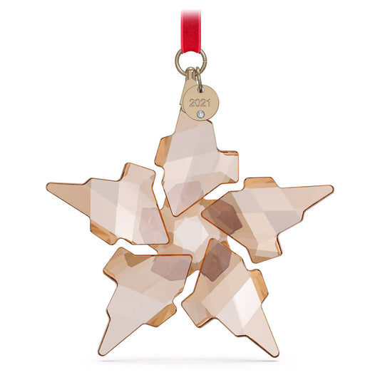 The Swarovski Festive Annual Edition 2021 Ornament by Swarovski showcases an elegantly hanging crystal snowflake with a faceted design. Accompanied by a red ribbon and a small round tag engraved with "2021," this beautiful crystal piece reflects a warm, amber hue.