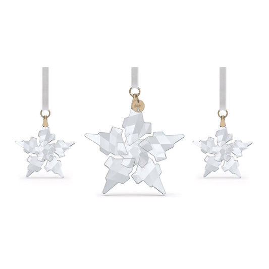 The Swarovski Annual Edition 2021 Ornament Set from Swarovski features three exquisite crystal star-shaped ornaments suspended from white ribbons. The central ornament is larger, adorned with intricate facets and a small gold tag inscribed with "2021." These dazzling stars reflect light beautifully, embodying the artistry of crystal craftsmanship for a graceful festive touch.