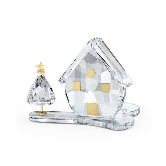 The Swarovski Holiday Magic Tea Light Holder Home Décor, designed by Swarovski, features a stunning crystal glass ornament depicting a small house with a slanted roof and gold square windows. Accompanying the house is an elegantly styled Christmas tree crowned with a gold star. The base is crafted to resemble a snowy landscape, making it an exquisite choice for use as an elegant tealight holder.