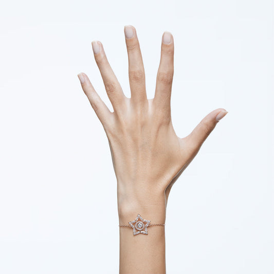 A hand is raised with fingers spread against a plain background, showcasing the exquisite Swarovski Stella Bracelet, adorned with a star-shaped charm and crafted in a rose gold-tone, encircling the wrist.
