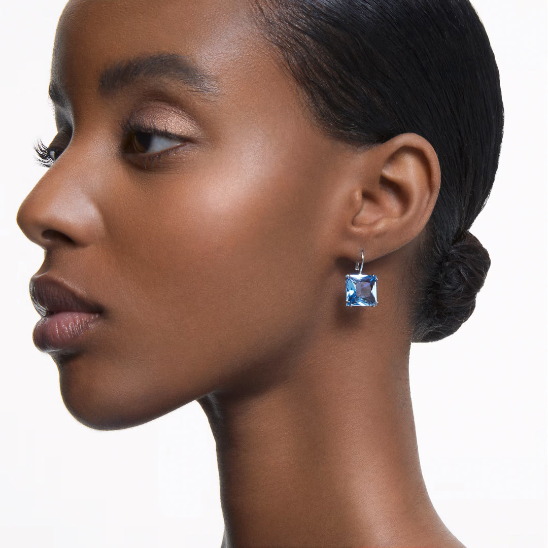 A woman in profile, showcasing smooth, glowing skin and a sleek bun, wears the large Swarovski Millenia Drop Earrings by Swarovski. The background is plain white, highlighting her elegant and minimalistic style.