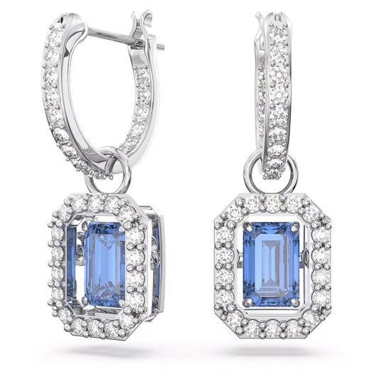 Close-up of the sophisticated Swarovski Una Drop Earrings, showcasing rectangular blue gemstones reminiscent of a dancing stone. These gemstones are encircled by shimmering white pavé crystals, with the drop design elegantly suspended from a circular hoop adorned with stones.