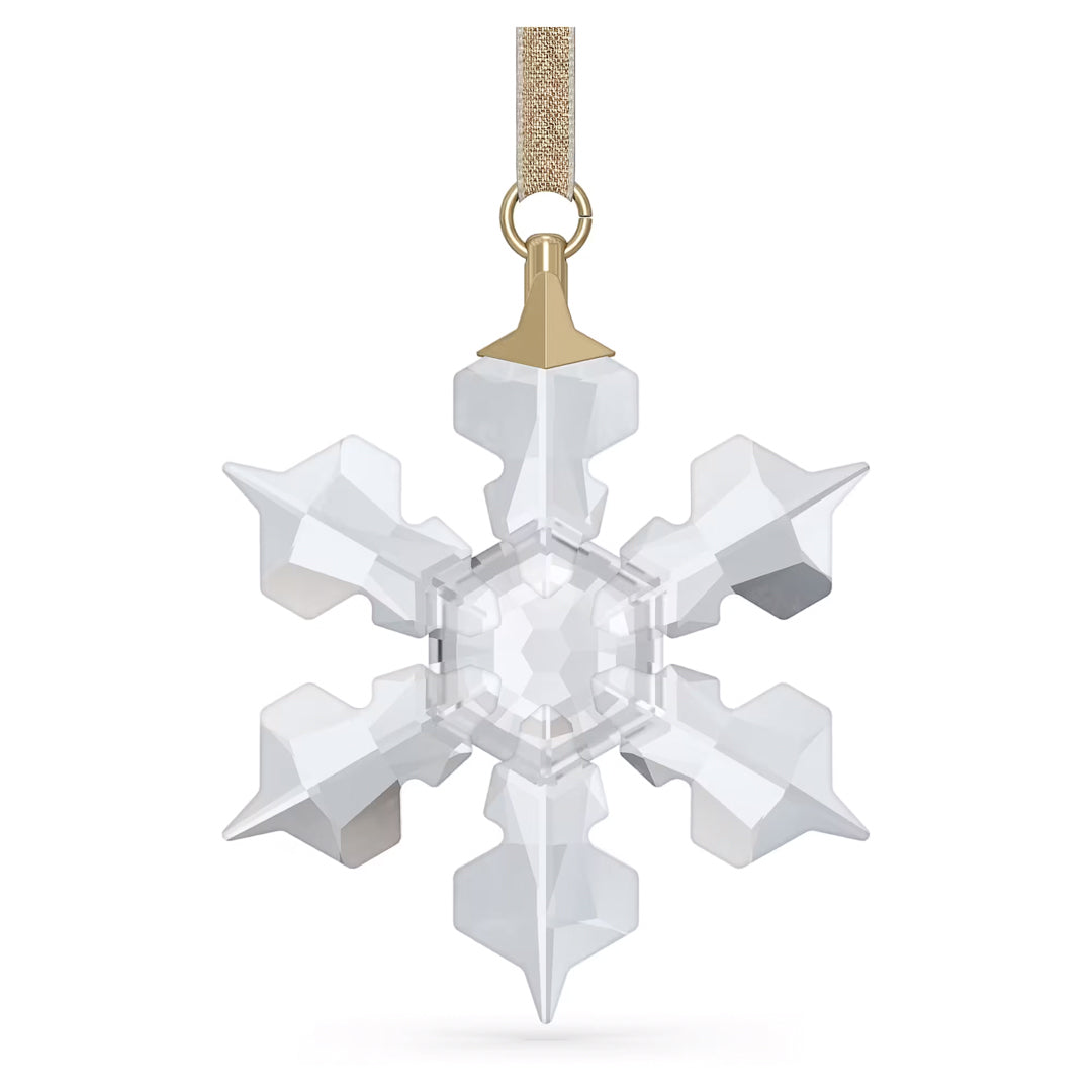 The Swarovski Little Snowflake Ornament Home Décor, featuring crystal facets and six shimmering points, hangs elegantly from a gold ribbon. Its clear, geometric design captures and reflects light, creating a dazzling sparkle.