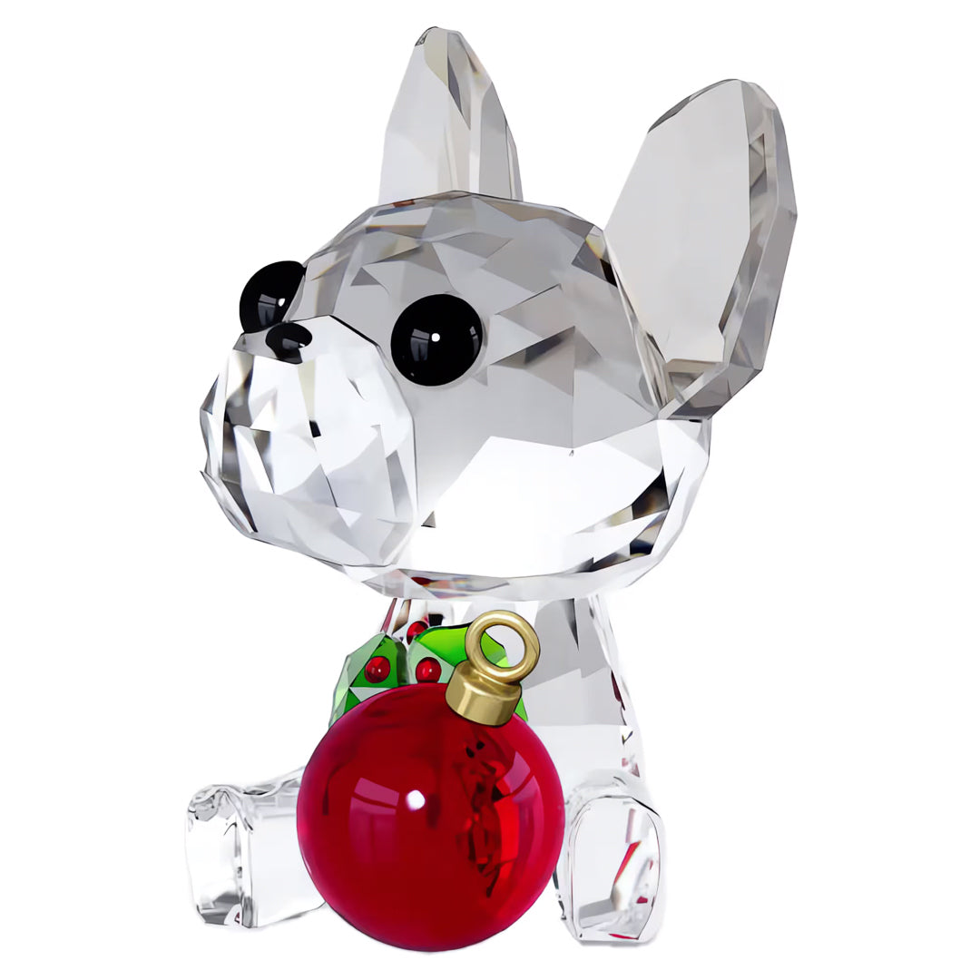 The Swarovski Holiday Cheers French Bulldog Home Décor piece, from the esteemed brand Swarovski, features a crystal sculpture of a French Bulldog with large black eyes, a red collar embellished with a green ornament, and it holds a festive red bauble. Its faceted and reflective surface captures light beautifully, making it an exquisite centerpiece for the holiday season.