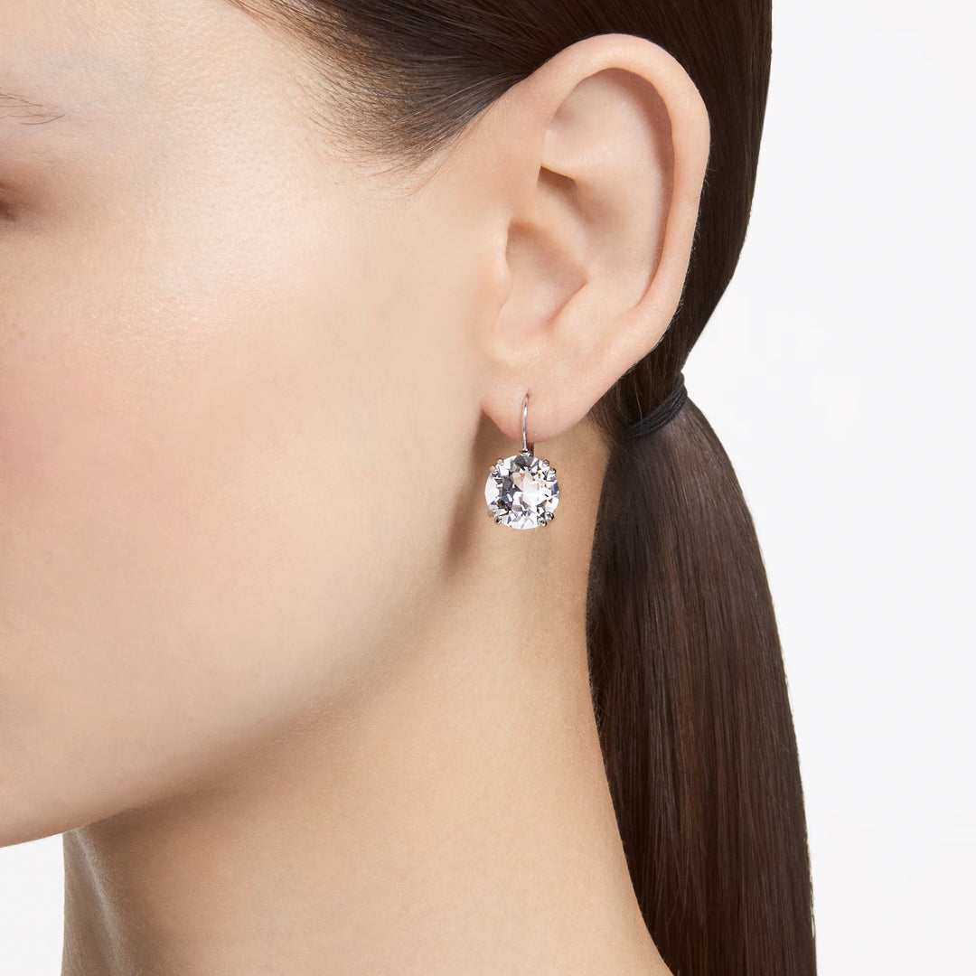 A close-up of a person wearing Swarovski's Millenia Drop Earrings. The rhodium-plated earrings, featuring a dazzling and round diamond design, catch the light beautifully and stand out as the focal point with hair elegantly pulled back.
