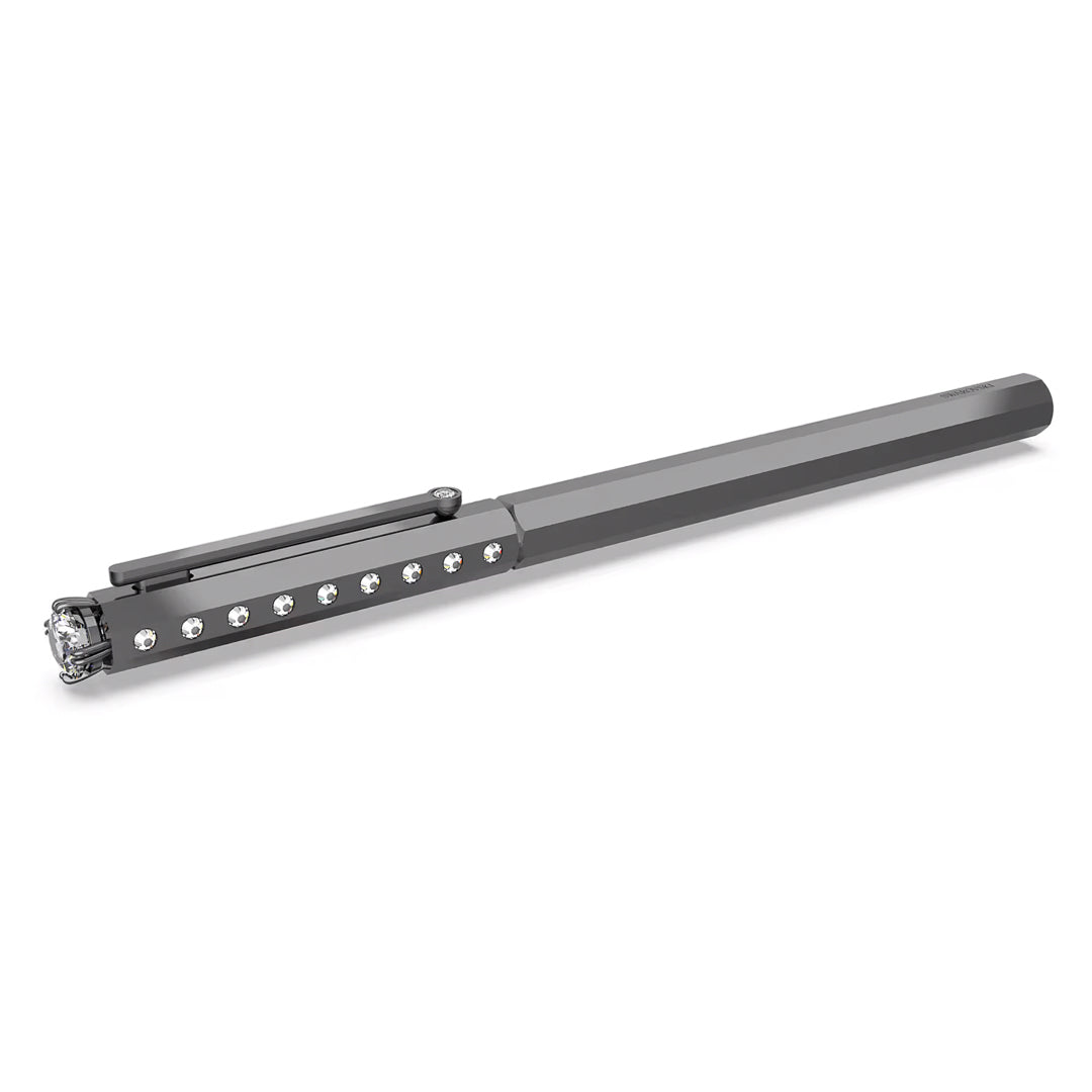 The Swarovski Ballpoint Pen, a product of Swarovski, boasts a sleek metallic appearance with a flat, elongated design and a cap clip. It is elegantly adorned with small crystals embedded along its side and offers a reflective, shiny finish, making it an exquisite addition to the Millenia Family.