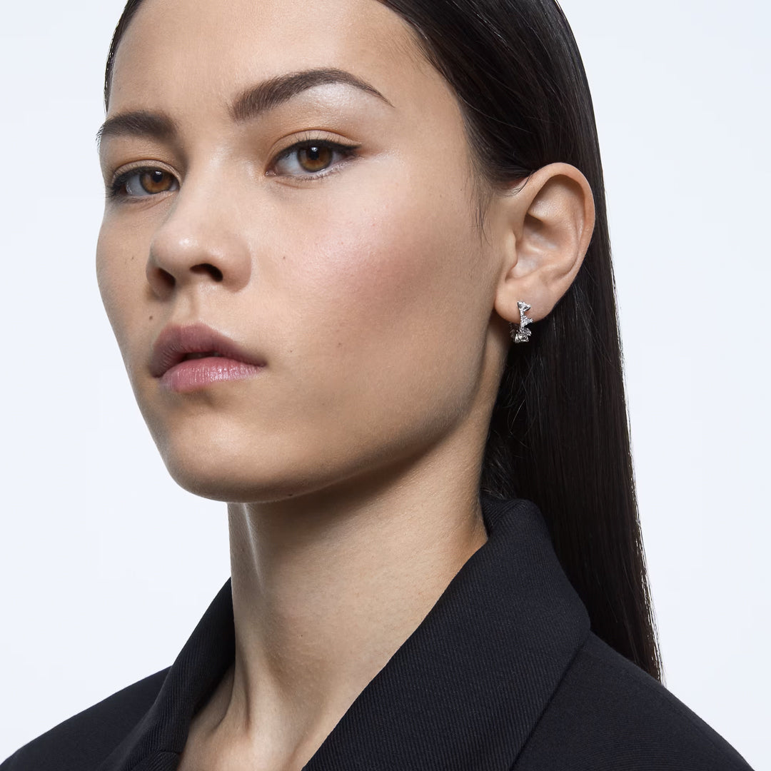 A person with long dark hair is wearing a black top and eye-catching Swarovski Matrix Hoop Earrings. They are looking slightly to the side against a plain light background.