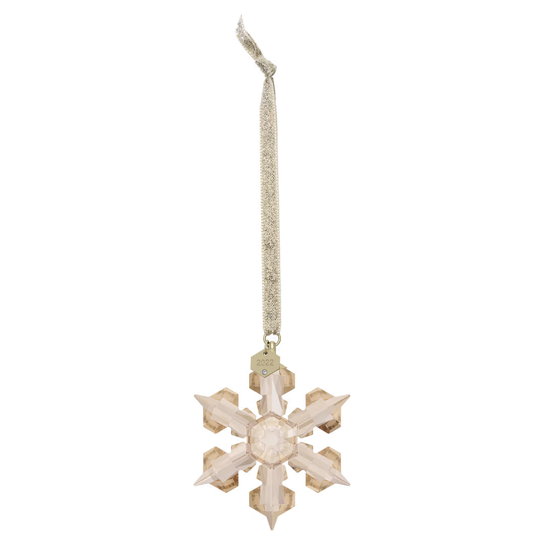 The Swarovski Festive2022 Annual Edition Ornament Home Décor, produced by Swarovski, is an exquisite crystal snowflake with intricate facets. It dangles from a shimmering ribbon and adds a stunning touch to holiday decorations. A small metal tag at the top bears the year "2022," making it an ideal piece for any collectible crystal star collection.