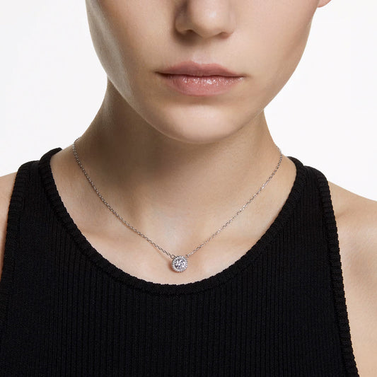 A person wearing a black sleeveless top showcases the sophistication of the Swarovski Una Angelic Necklace Pendant, a delicate silver piece featuring a stunning circular Swarovski pendant. The plain white background highlights the jewelry's brilliance beautifully.